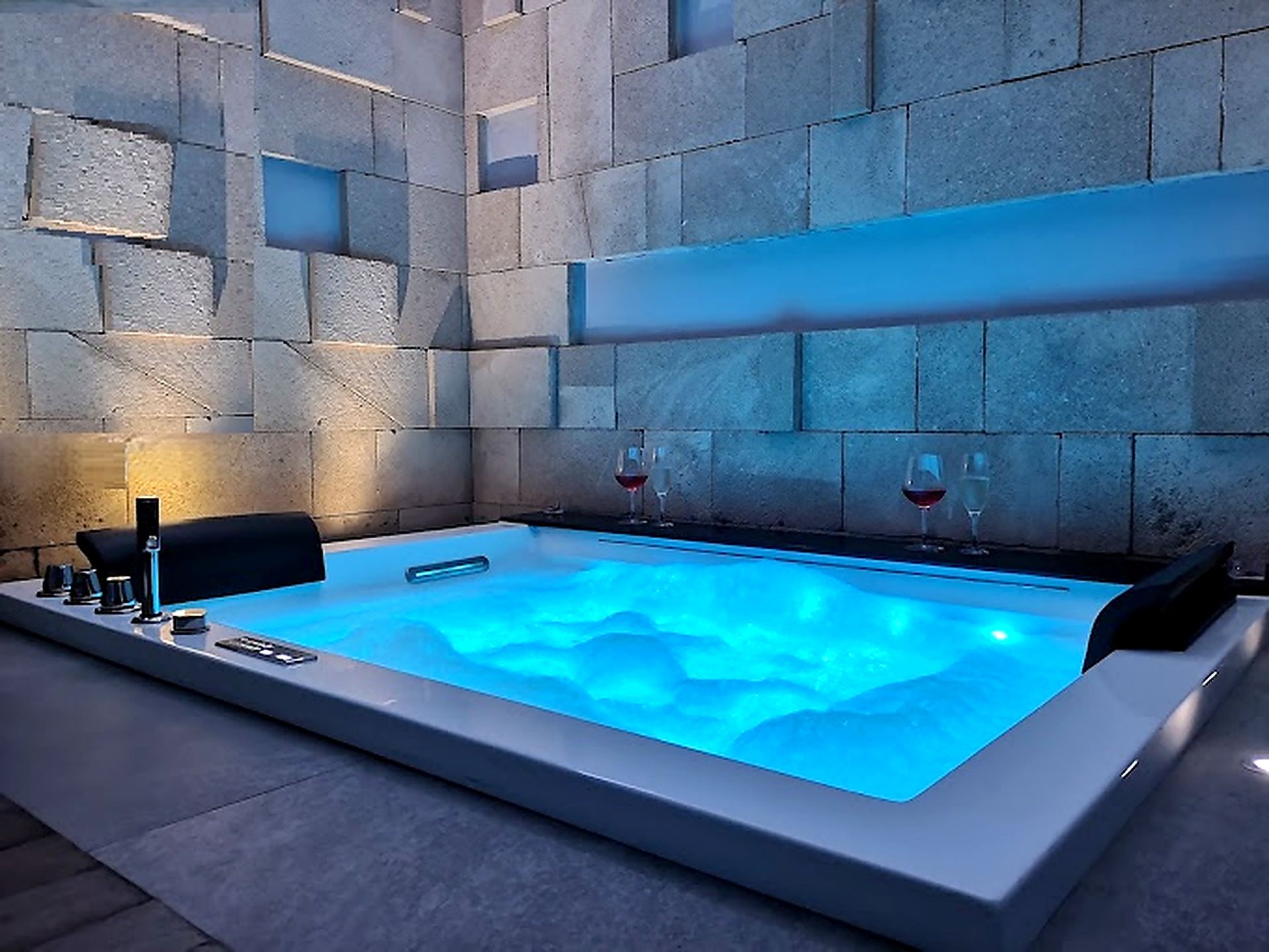 La baignoire balnéo pour deux de la suite, éclairée en bleu clair par la chromothérapie, deux verres de vin sur le rebord