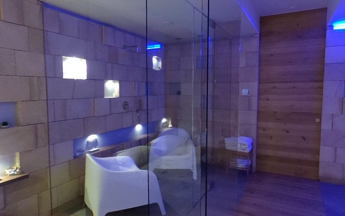 Aperçu de la visite à 360 degrés de la suite : l'espace détente en verre avec fauteuils blancs et lumière bleue